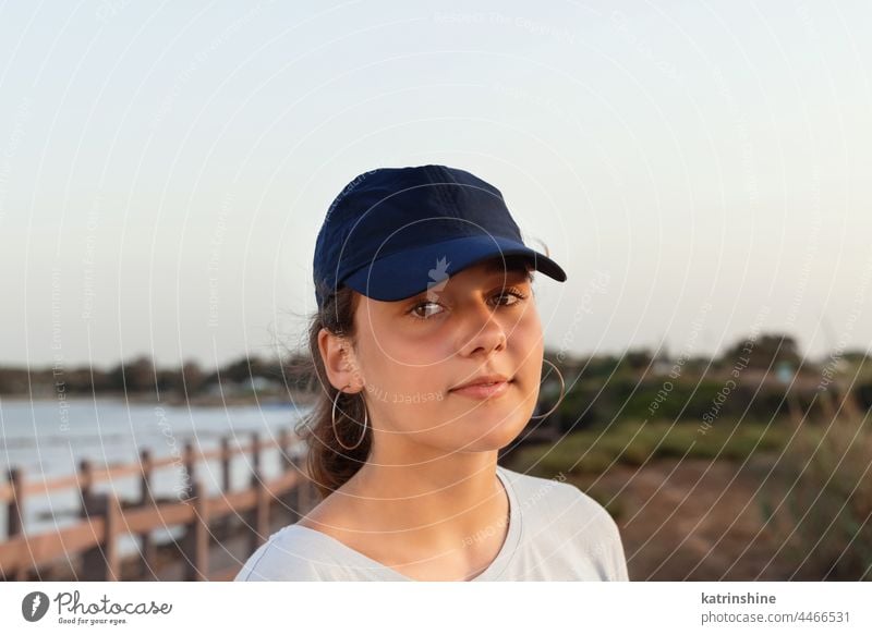 Teenager-Mädchen mit dunkelblauer Baseballmütze steht bei Sonnenuntergang am Meer. Kappe Mockup im Freien Jugendlicher Kaukasier Attrappe MEER visier tragend