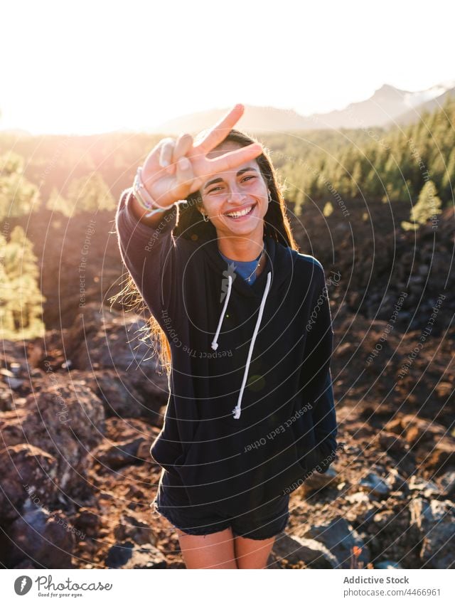 Lächelnder Teenager mit Friedensgeste gegen einen Berg im Sonnenlicht zwei Finger Sieg v-Zeichen cool Berge u. Gebirge freundlich Porträt genießen herzlich