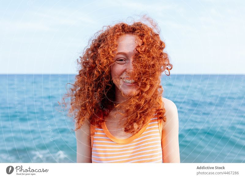 Fröhliche Frau am Meeresufer stehend Glück blau MEER Wind Ufer froh Urlaub Feiertag Freude heiter lange Haare Rotschopf Wasser Natur Optimist Ingwerhaar positiv