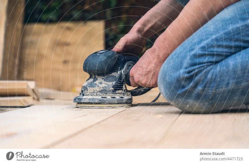 Nahaufnahme eines Arbeiters, der Holzbretter mit einer Schleifmaschine schleift Schleifmittel Arme Kabel Zimmerer Schreinerei Konstruktion Handwerk Staubwischen