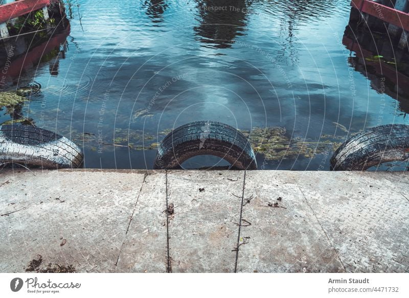 drei alte Autoreifen als Rammschutz in einem kleinen Hafen Verlassen Hintergrund PKW Beton Konstruktion Detailaufnahme Schmutz Grunge hafen See Landen