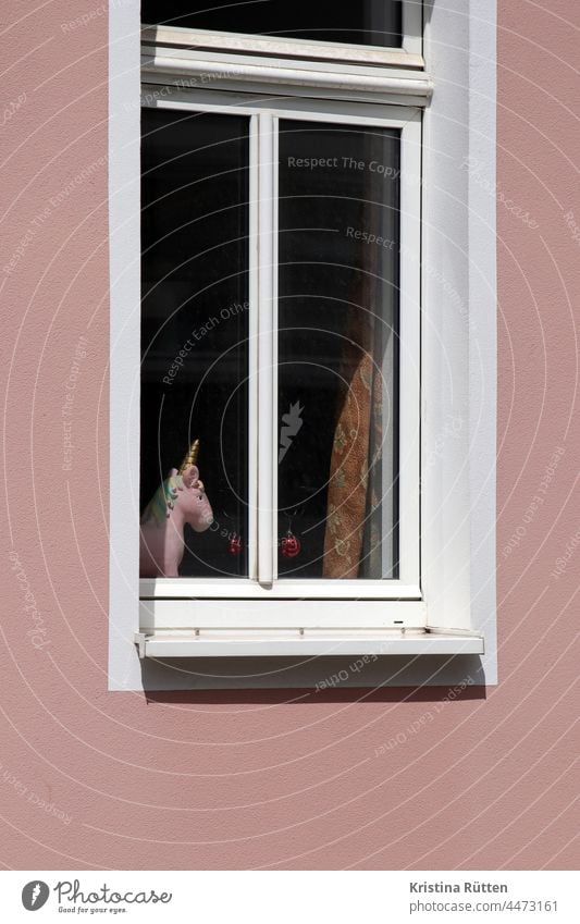 rosa einhorn mit goldenem horn steht im fenster fabelwesen fensterbank einblick aussicht ausblick vorhang gardine weihnachtsbaumkugeln christbaumkugeln