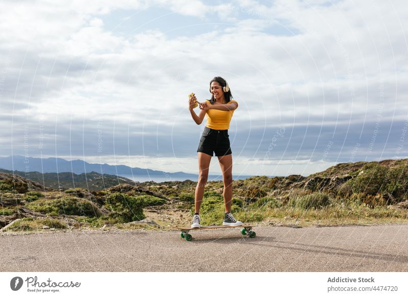 Lächelnde ethnische Frau auf Longboard und Selfie machen Glück Kopfhörer zuhören benutzend Musik Smartphone Freizeit Optimist Aktivität Hipster Hobby Gerät