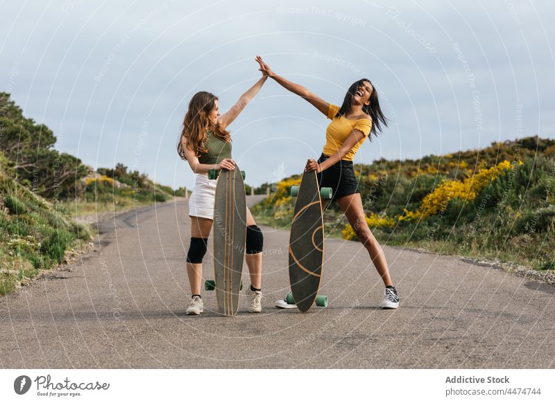 Fröhliche unterschiedliche Frauen geben sich auf der Straße die Klinke in die Hand Freund high five Longboard Glück Freundschaft Spaß genießen Hobby Gruß