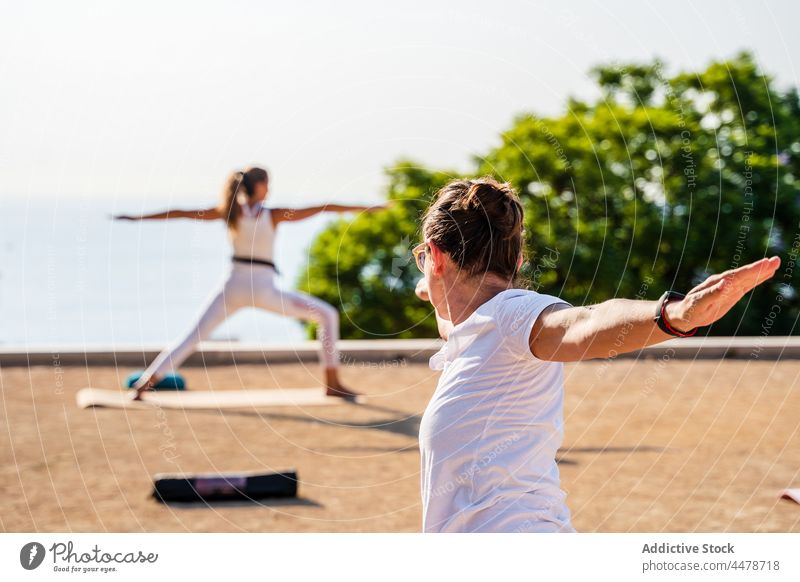 Frauen in der Position des Kriegers II während einer Yogasitzung im Park Ausbilderin virabhadrasana b Asana Wohlbefinden üben Zen Harmonie Arme hochgezogen