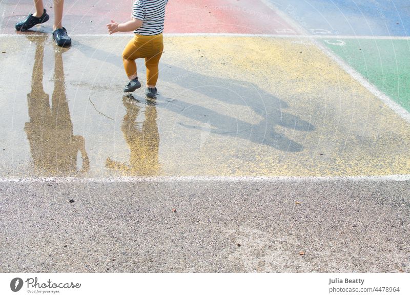 Bruder und Schwester stapfen in den Pfützen auf einem Schulhof; bunter 4-Quadrat-Platz und Schatten von Geschwistern platschen Vierkant Spielplatz Park