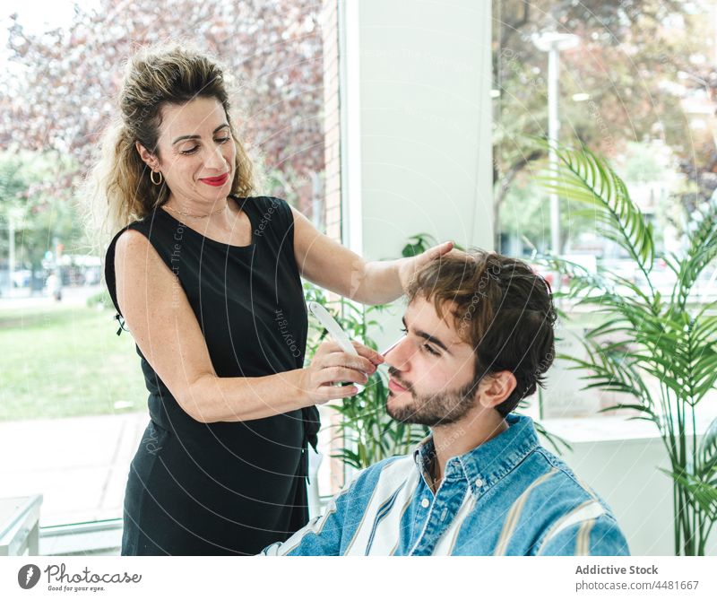 Frau schneidet männlichen Kunden im Salon Mann Friseur Meister Dienst geschnitten Klient Vollbart Fenster Inhalt Stil professionell Werkzeug Prozess Lächeln