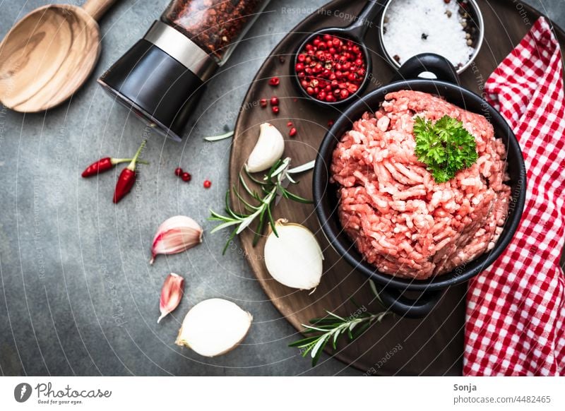 Rohes Hackfleisch in einem Topf und Zutaten auf einem grauen Tisch roh Vorbereitung gewürz Pfeffermühle Essen zubereiten Küche Gewürz Gesundheit frisch