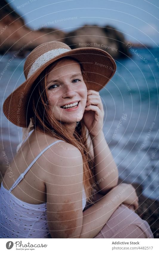 Lächelnde Frau mit Hut am Strand MEER Sommer Glück Wasser Küste Natur Ufer sitzen charmant jung trendy Vergnügen friedlich froh Kopfbedeckung Seeküste Vorschein