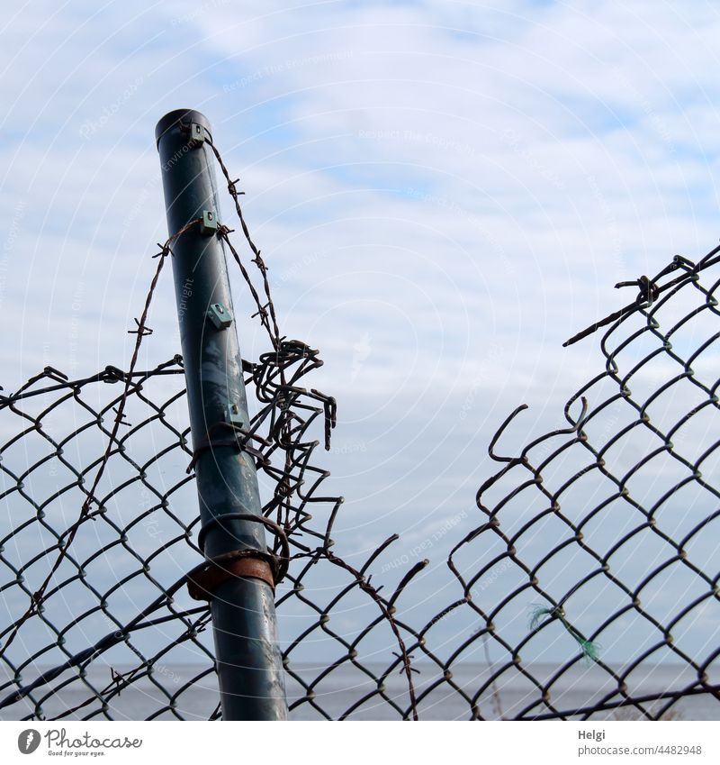 kaputt - zerstörter Maschendrahtzaun mit Metallpfahl und Stacheldraht vor blauem Himmel mit Wolken Zaun Maschendrahtzaum Pfahl Nordsee Insel Schutz Sicherheit