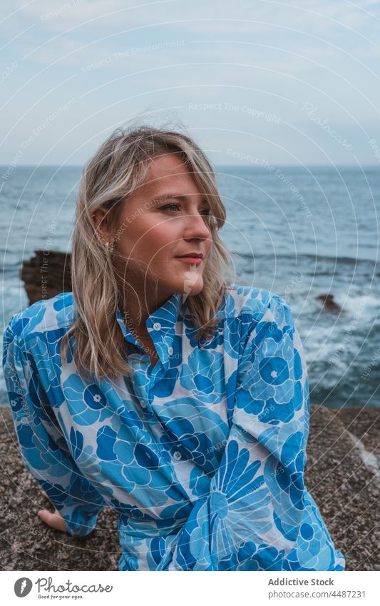 Nachdenkliche Frau, die gegen den blauen Ozean am Abend wegschaut nachdenklich Meer Felsen besinnlich verträumt ruhig charmant Stil Windstille donostia