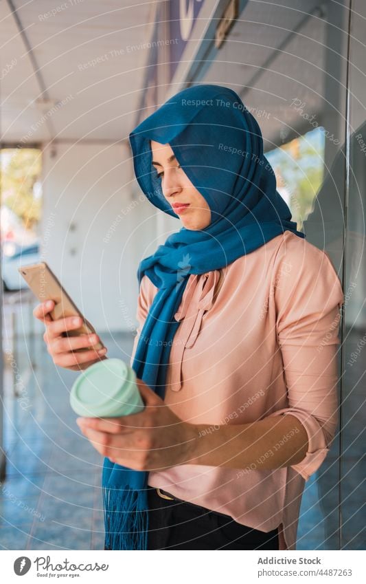 Muslimische Frau mit Kaffee zum Mitnehmen und Smartphone Imbissbude Großstadt Browsen Hijab Mobile Telefon ethnisch arabisch muslimisch Straße online Nachricht