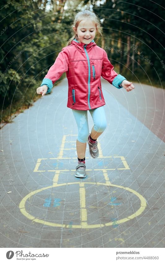 Aktives kleines Mädchen spielt Himmel und Hölle auf einem Spielplatz im Freien springend Spielen schwofen Vorschule Kind Spaß Kreide spielen außerhalb Übung