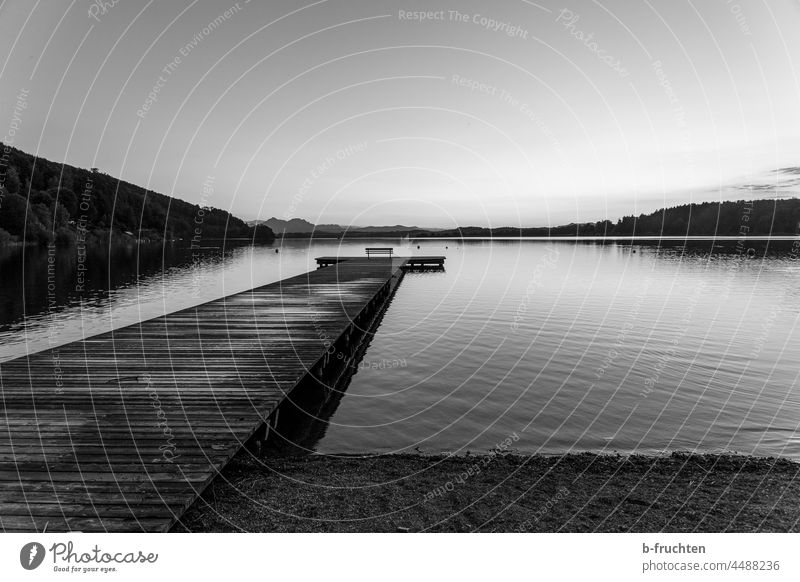 ruhige, einsame Stimmung am See, Holzsteg mit Sitzbank. Wallersee Ruhe Herbst stille Parkbanksitzen stiller Moment Abendstimmung Landschaft Schwarzweißfoto