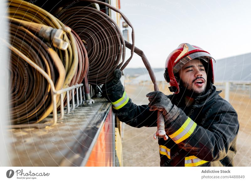 Feuerwehrmann, der einen Feuerwehrschlauch aus dem Fahrzeug zieht Schlauch Schutzhelm Ackerland Gerät retten Landschaft Beruf Mann Lastwagen Uniform Sicherheit