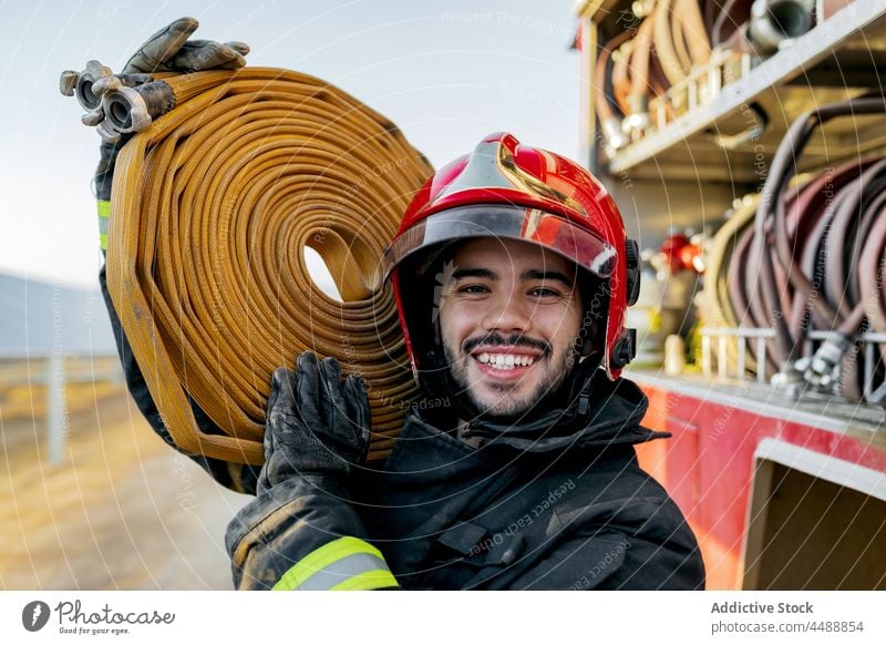 Feuerwehrmann trägt Feuerwehrschlauch auf der Schulter Schlauch Schutzhelm Ackerland Gerät retten Landschaft Beruf Mann Lastwagen Uniform Sicherheit männlich