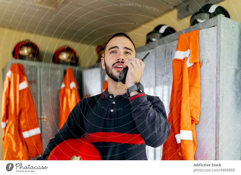 Junger Feuerwehrmann spricht ins Funkgerät professionell Uniform Kommunizieren Arbeitsbekleidung Spind sprechen Notfall Bericht Mann Beruf Handfunkgerät