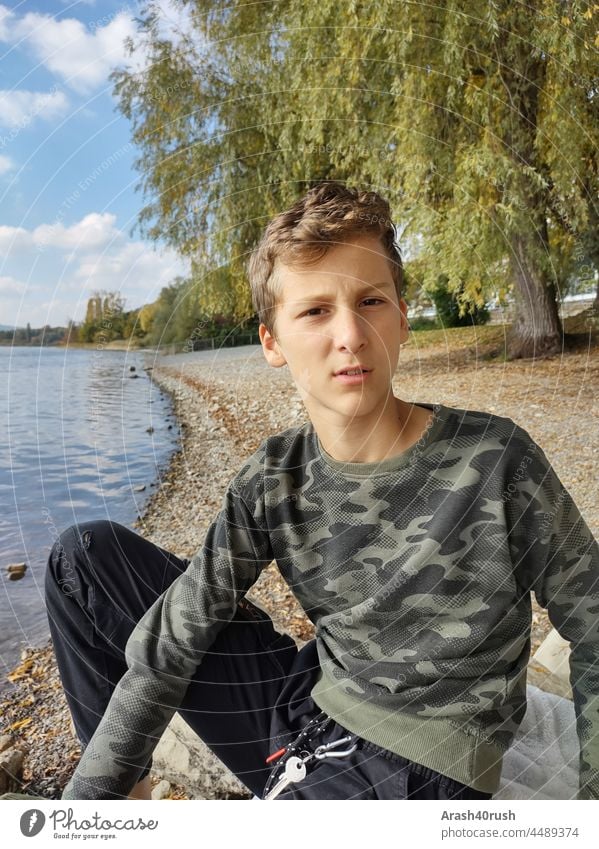 Lausbub mit skeptischem Blick Junge Teenager am See Außenaufnahme chillig Vorderansicht Ufer Wasser Natur Farbfoto Erholung ruhig Menschenleer Wasseroberfläche