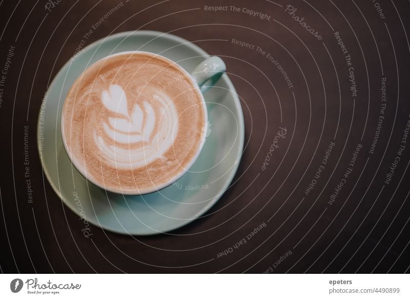 Draufsicht auf eine Tasse mit schaumigem Kaffee auf einem dunklen Tisch braun Café Cappuccino Capuccino Textfreiraum flache Verlegung Blume Bierschaum grün Herz