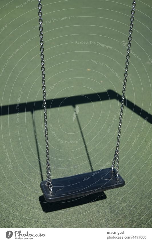 Leere Schaukel auf Kinderspielplatz grün schwarz Spielplatz menschenleer verlassen spielen Außenaufnahme Kindheit Lockdown schaukeln trist Lebensfreude