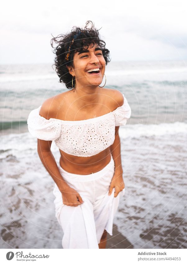 Fröhliche ethnische Frau am Meer im Sommer Meeresufer weiß Outfit Lachen Spaß haben MEER Strand heiter Augen geschlossen Stil krause Haare Küste Freude positiv