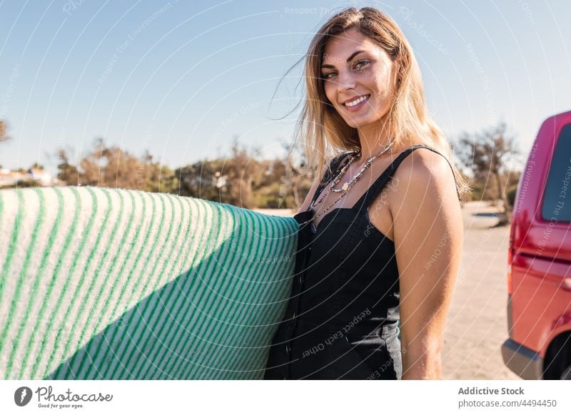 Lächelnde Frau mit Surfbrett am Ufer Sportlerin Strand Meeresufer Surfer Deckung Tasche Hobby Küste Wassersport Sommer Gerät Urlaub Erholung behüten tropisch