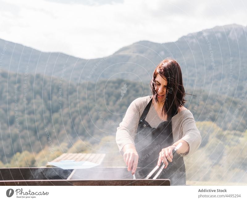 Frau brät Würstchen auf dem Grill auf dem Lande Koch Wurstwaren Fleisch Grillrost Barbecue Braten Landschaft Gitter Feld grillen Lebensmittel geschmackvoll