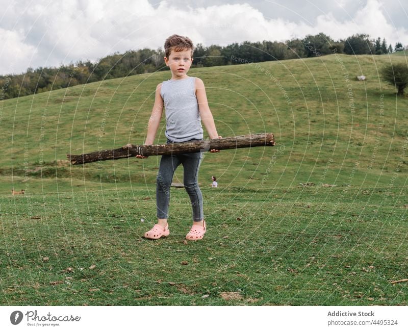 Junge mit Baumstamm auf einer Wiese stehend Kind Hügel Totholz Strahl Landschaft Kindheit Zeitvertreib Freizeit Feld ländlich Sommer Erholung Berge u. Gebirge