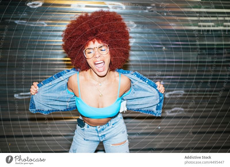 Stilvolle Frau in Jeansjacke Straße Afro-Look Mode trendy Bekleidung Outfit Abend Jacke anhaben dunkel Dämmerung Vorschein Frisur Sonnenbrille Accessoire