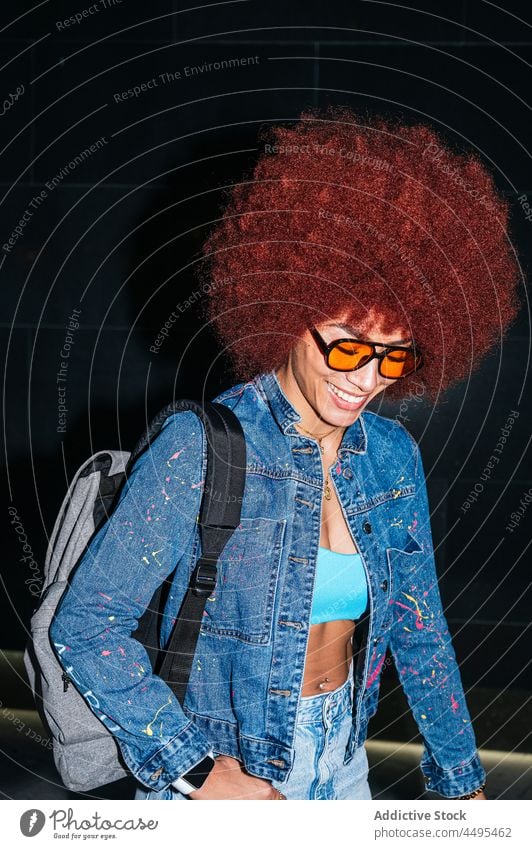 Glückliche Frau in stilvoller Kleidung auf dunkler Straße Jeansstoff Afro-Look Stil Mode Bekleidung Streetstyle Rucksack Abend anhaben dunkel Dämmerung Frisur