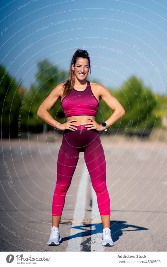 Fröhliche Sportlerin auf Asphalt mit den Händen auf der Hüfte Frau passen Fitness Sportbekleidung Training sportlich schlank Zahnfarbenes Lächeln Sportkleidung