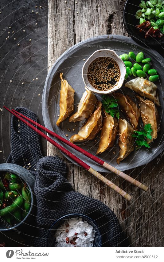 Gyozas mit Bohnen und Soße in der Nähe von Gewürzen und Erbsenschoten Sojasauce Schalen & Schüsseln Essstäbchen Mahlzeit Lebensmittel Mittagessen Samen Sesam