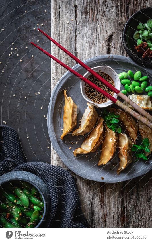 Gyozas mit Bohnen und Soße in der Nähe von Gewürzen und Erbsenschoten Sojasauce Schalen & Schüsseln Essstäbchen Mahlzeit Lebensmittel Mittagessen Samen Sesam