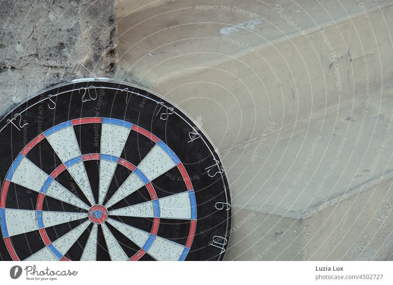 oft getroffen: eine alte Dartscheibe lehnt an einer Treppe, als Sperrmüll bereitgestellt Treffer Spiel Löcher aussortiert Ziffern Zahlen rot blau weiß