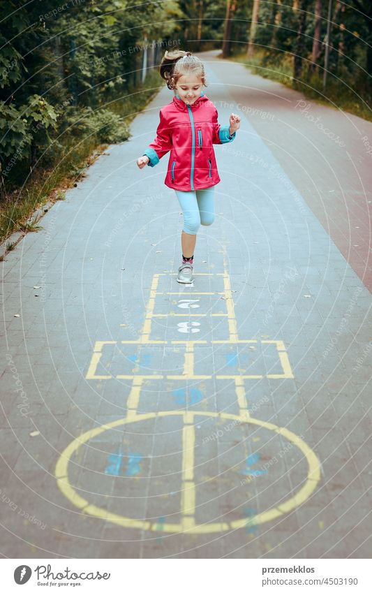 Aktives kleines Mädchen spielt Himmel und Hölle auf einem Spielplatz im Freien springend Spielen schwofen Vorschule Kind Spaß Kreide spielen außerhalb Übung