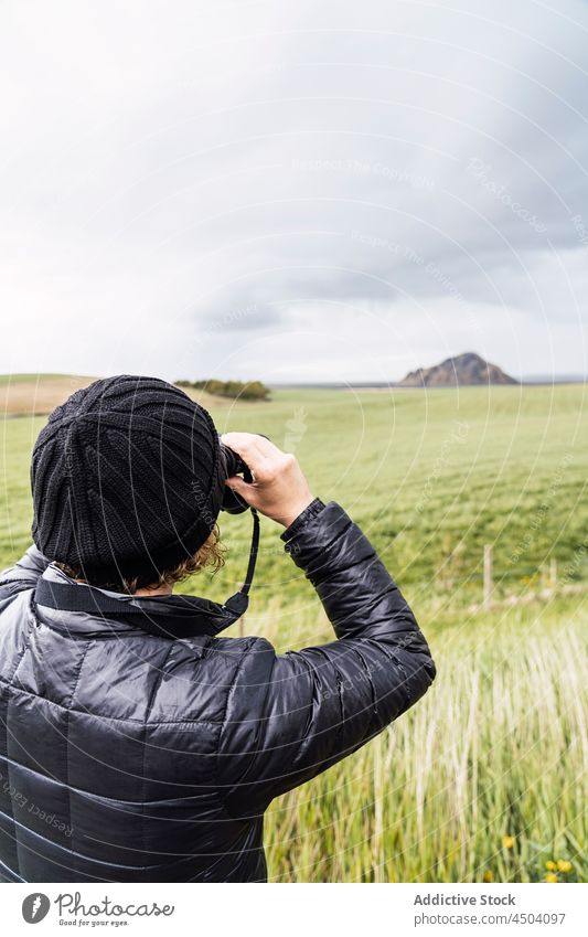 Anonymer männlicher Reisender, der mit einer Fotokamera auf einer Wiese stehend die Natur fotografiert Mann fotografieren Berge u. Gebirge Fotoapparat erkunden