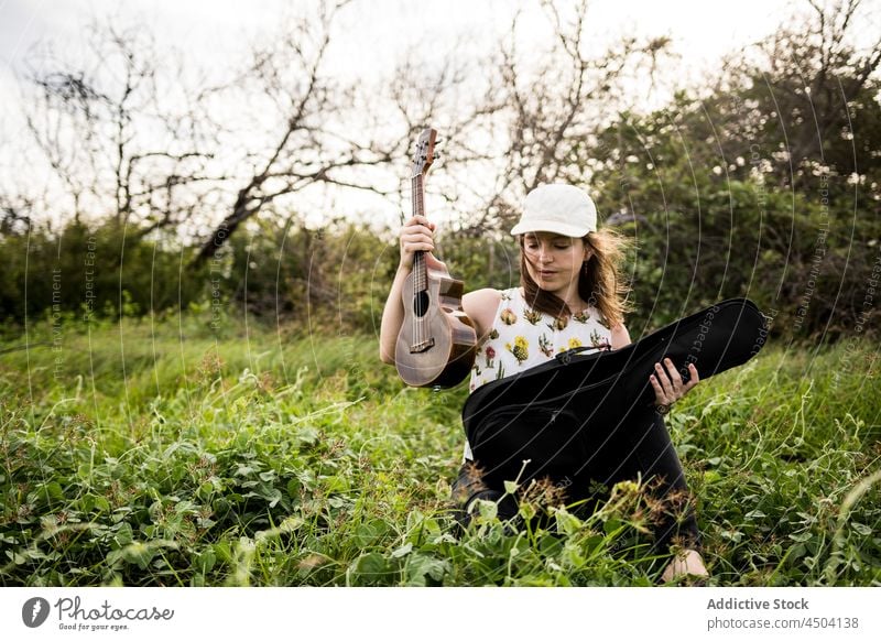 Musikerin öffnet Koffer mit Ukulele im Gras bei Tageslicht Frau offen Instrument Hobby sitzen Windstille Melodie Natur Gesang Klang Talent nachdenklich