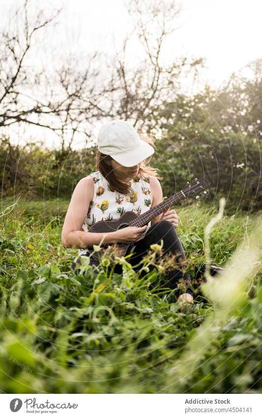 Musikerin spielt Ukulele in der Natur bei Tag Frau Instrument spielen Gras üben ausführen Hobby lässig sitzen Verschlussdeckel Tageslicht Windstille Stil