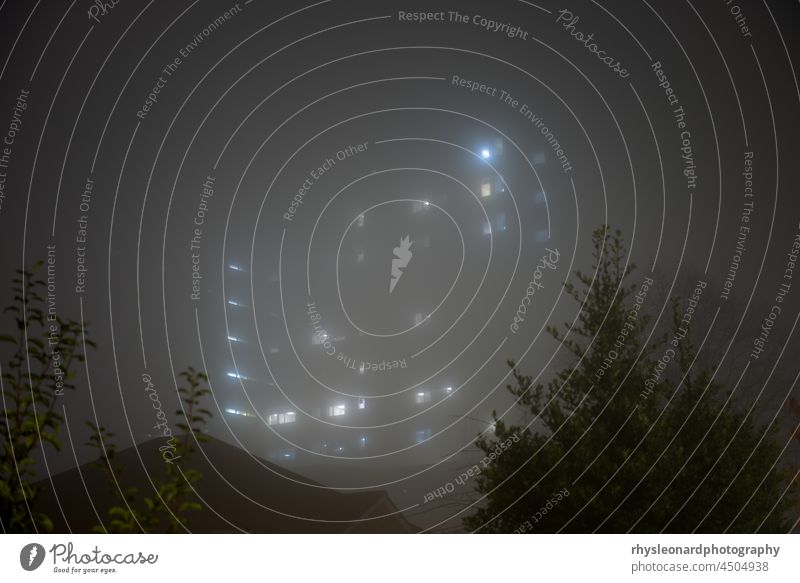 Unheimliche Sky Scraper Krankenhaus Lichter scheinen durch sehr dichten Nebel in der Nacht. Dunkles und geheimnisvolles hohes Gebäude. unheimlich Wolkenkratzer