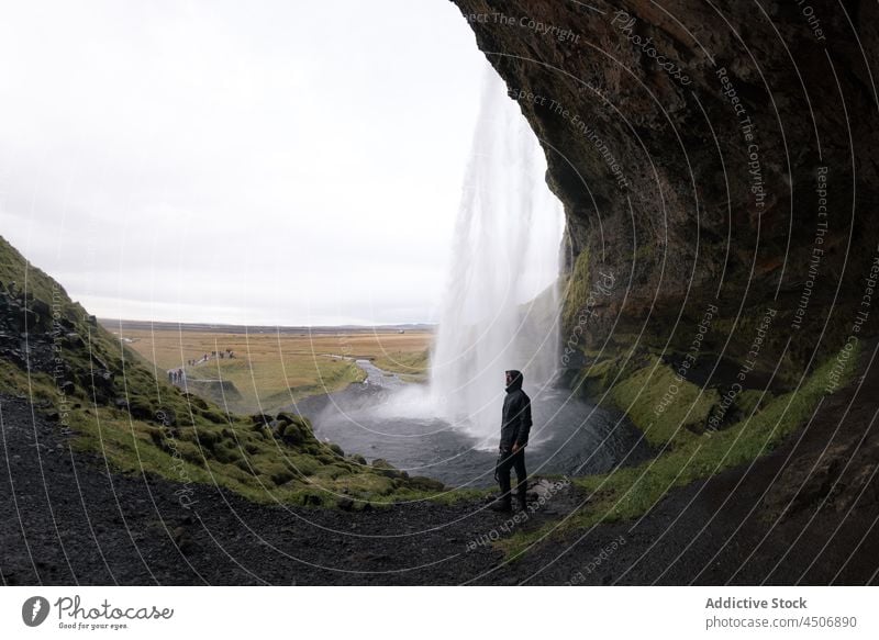 Unbekannter Mann steht in der Nähe eines reißenden Wasserfalls, der durch eine Felswand fließt Klippe Höhle bewundern Natur Kraft Reisender erkunden Landschaft