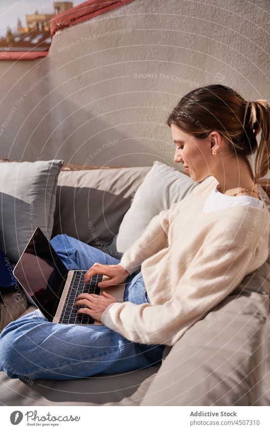 Frau mit Laptop auf der Terrasse benutzend Kälte Internet Dachterrasse online Tippen Gerät Netbook Browsen Sofa modern Beine gekreuzt Jeansstoff Flasche