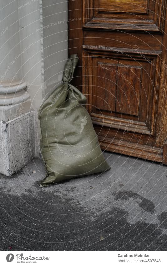 Grüner Sandsack steht vor einer Haustür als Schutz vor Hochwasser Tür Umwelt alt Eingang Gebäude Fassade Wand Mauer Menschenleer Außenaufnahme Farbfoto Bauwerk