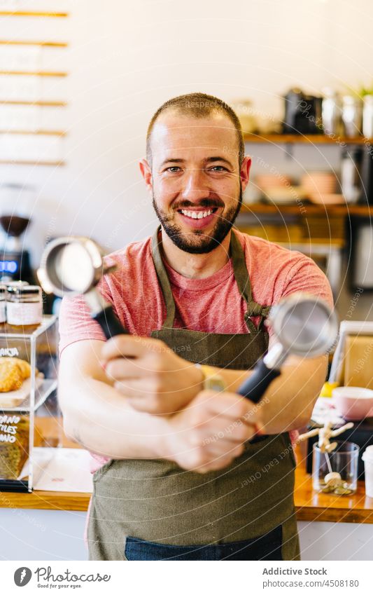 Gut gelaunte Barista mit Portafiltern in den Händen Mann Kaffeehaus Abfertigungsschalter Vorrichtung Vorrat Arbeit Dienst Gerät Personal professionell Kantine