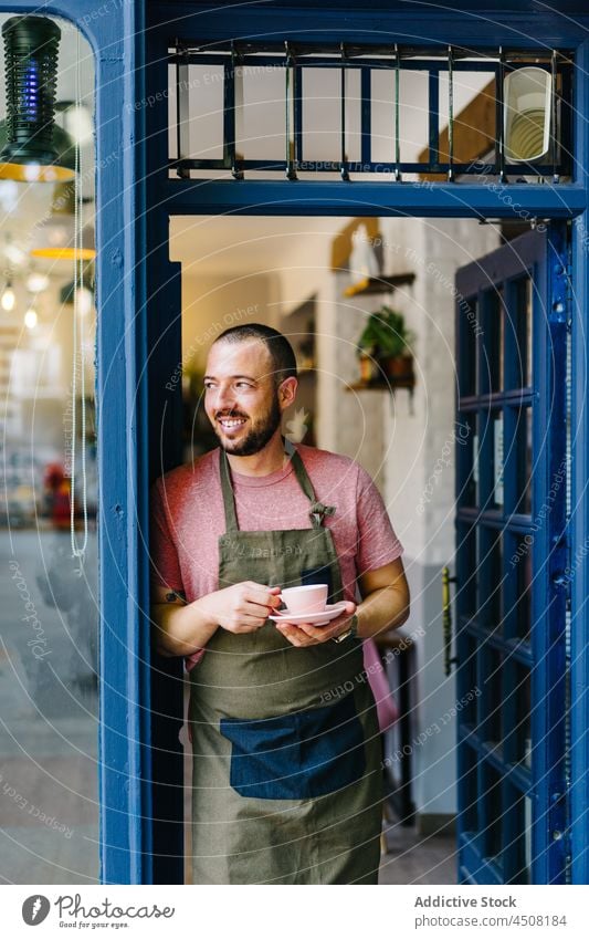 Gut gelaunte Barista mit Kaffee in der Tür stehend Mann Kaffeehaus Tasse Arbeit Türöffnung Eingang Heißgetränk Getränk Personal professionell Kantine Schürze