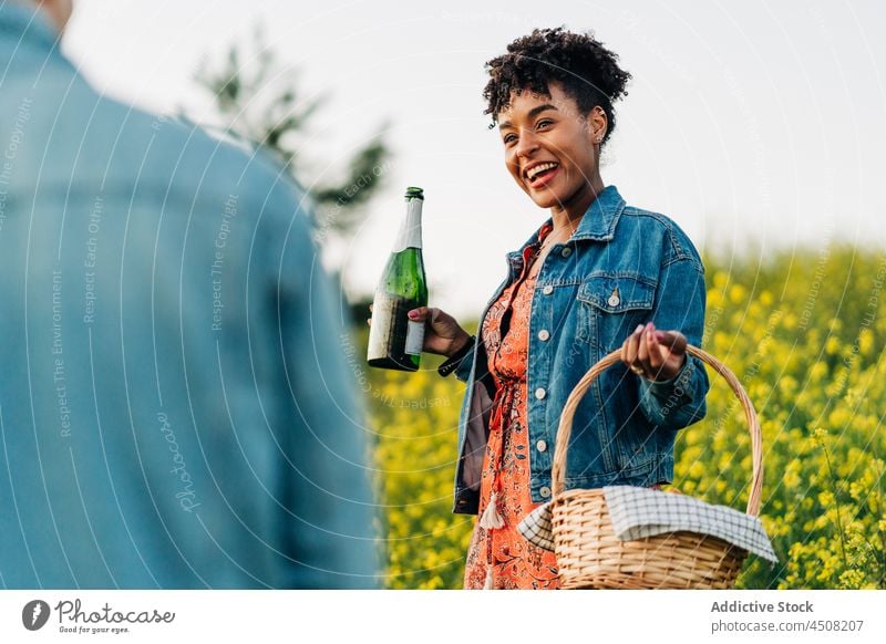 Glückliche ethnische Frau mit Champagnerflasche lächelnd mit Ernte Freund im Park Paar Liebe heiter feiern Natur romantisch Zusammensein Termin & Datum positiv