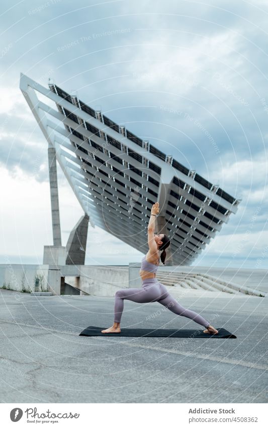 Frau macht Krieger Asana auf der Straße Yoga solar Panel Übung Training üben Energie beweglich Dame modern Gleichgewicht Sportbekleidung Wellness Achtsamkeit