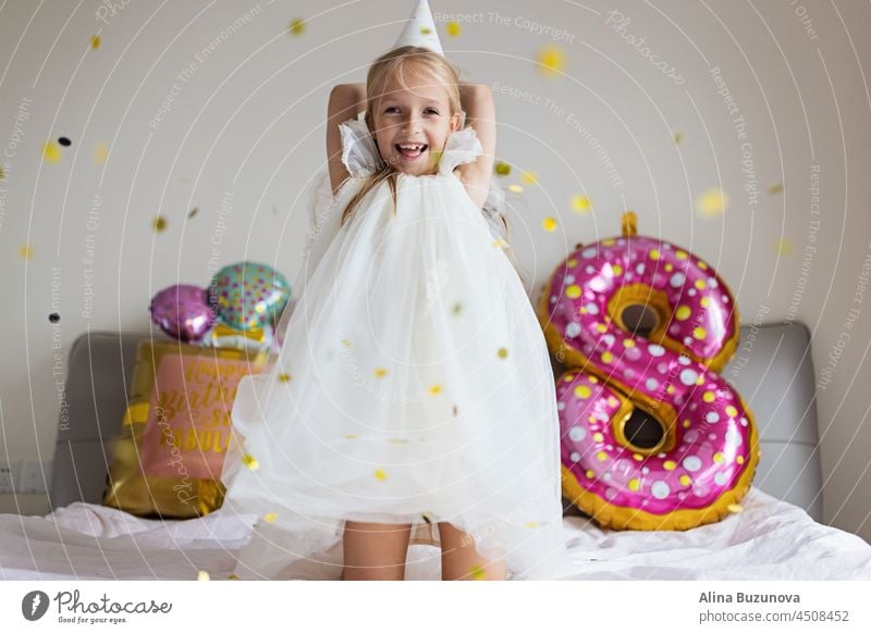 Cite kleinen kaukasischen Mädchen feiern acht Jahre alt Geburtstag zu Hause. Stylish Kid trägt modisches Kleid und haben Spaß mit Konfetti auf dem Bett