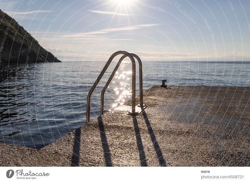 glitzernde Sternensonnenstrahlen auf dem Wasser hinter der Poolleiter am Meer glänzend h2o Laufmasche liquide MEER Schwimmsport Baden Textfreiraum Tauchen Tropf