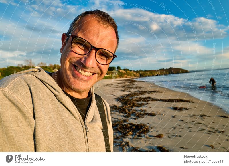 Mann mittleren Alters mit Brille lächelnd glücklich am Strand, Herbsttag Lebensmitte Kaukasier kaukasische Ethnizität 40s 40-45 Jahre Lächeln