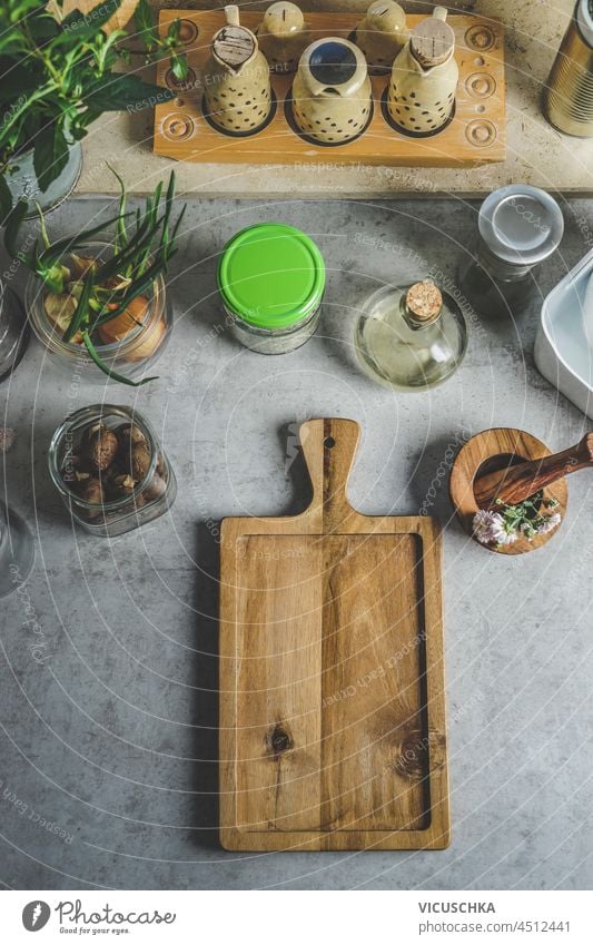 Lebensmittel Hintergrund mit hölzernen Schneidebrett, Mörser und Stößel, Gläser mit Zutaten und Kräutern auf grauen Küchentisch. Kochen zu Hause mit plastikfreien Küchenutensilien. Draufsicht mit Kopierbereich.